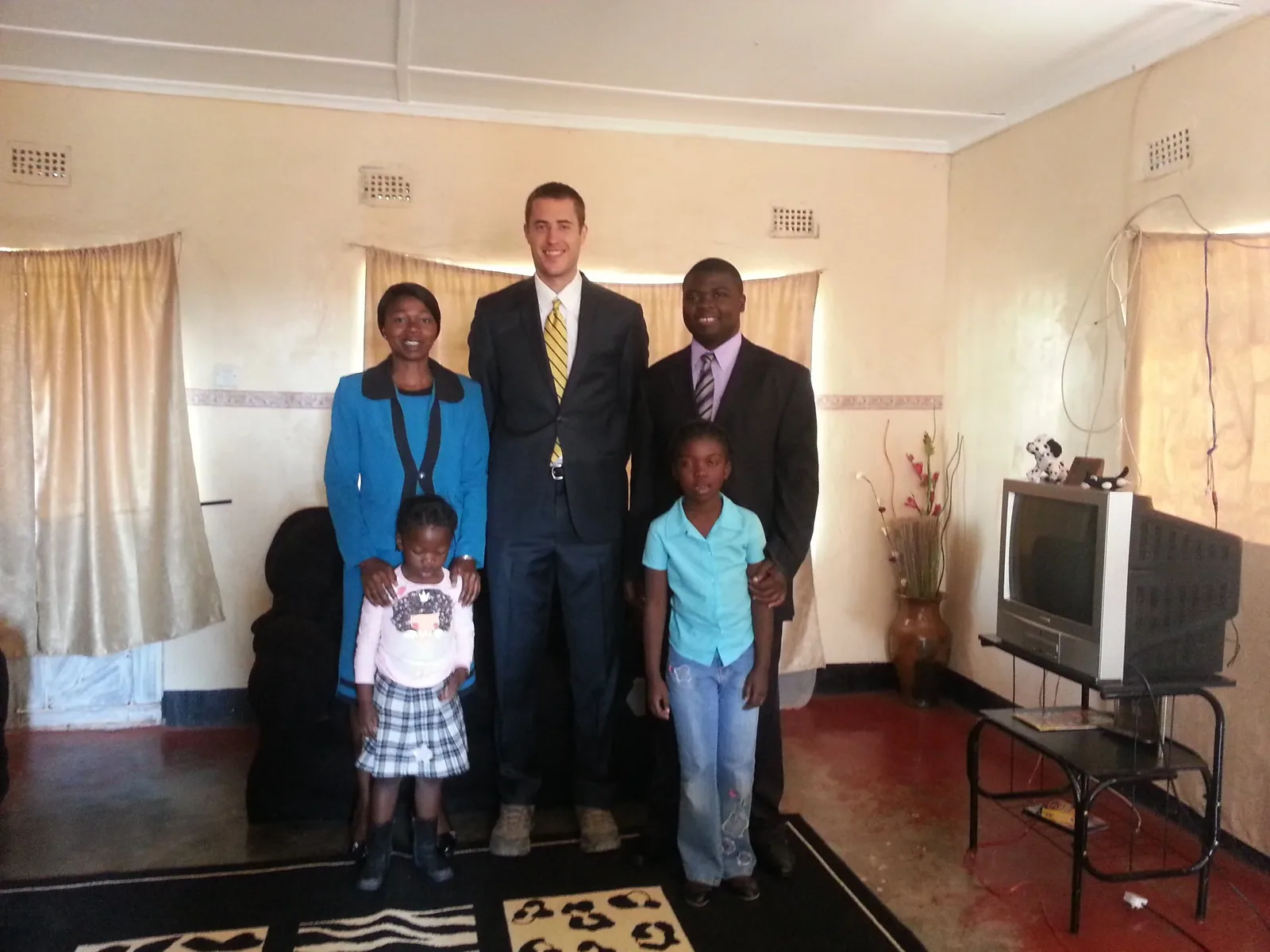 A family standing with a visiting JPBC member in the front room of their home