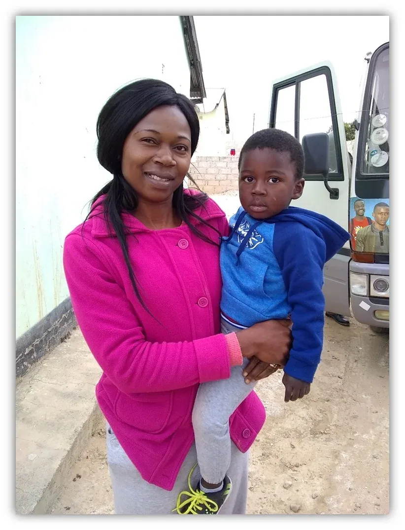 A mother in a bright pink coat holding her young son beside a truck