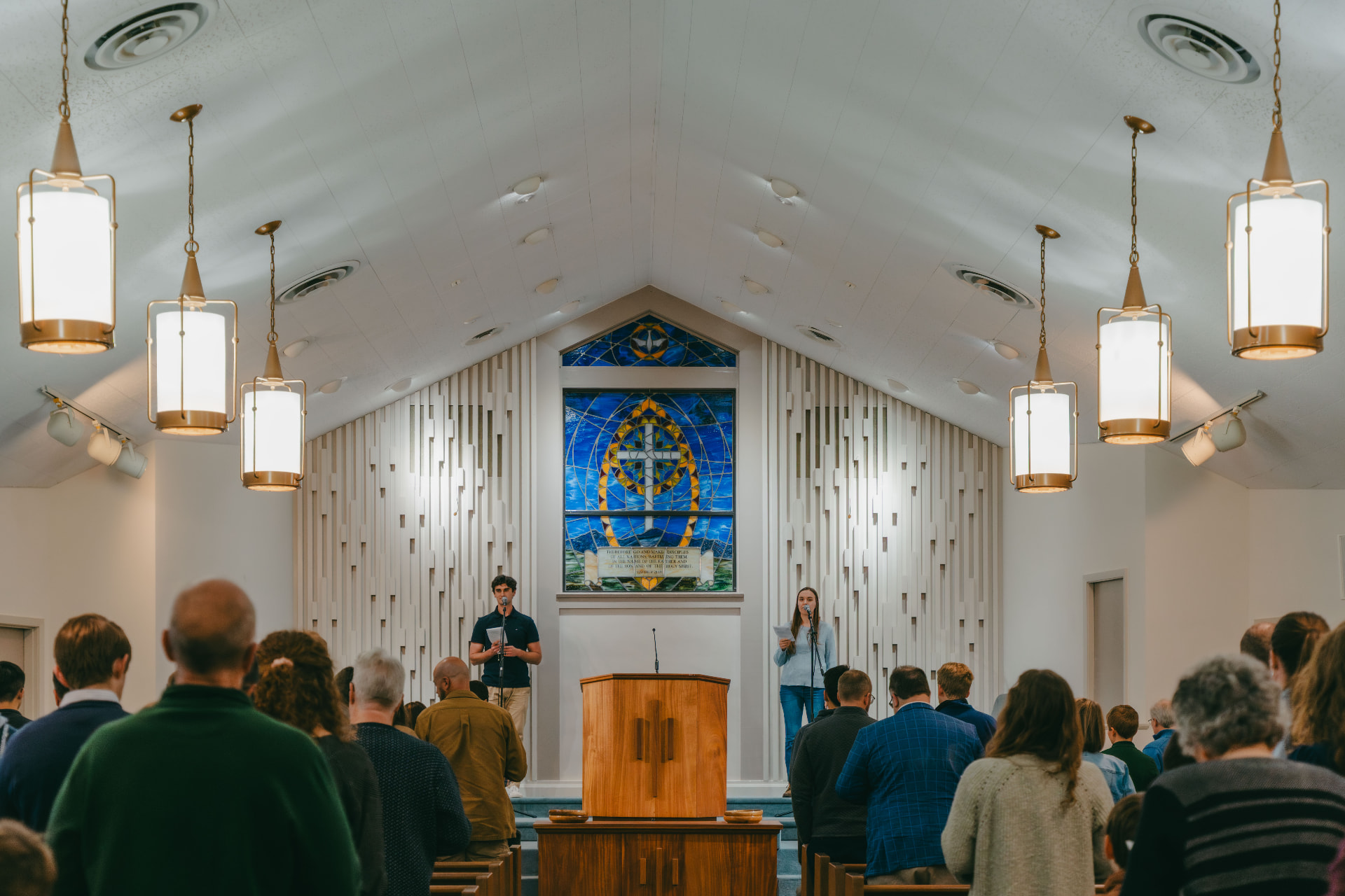 The congregation of Jefferson Park Baptist Church standing in worship beneath the stained glass cross window