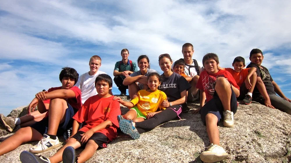 Southwood kids and leaders sitting together on a rocky summit under a blue sky after a hike