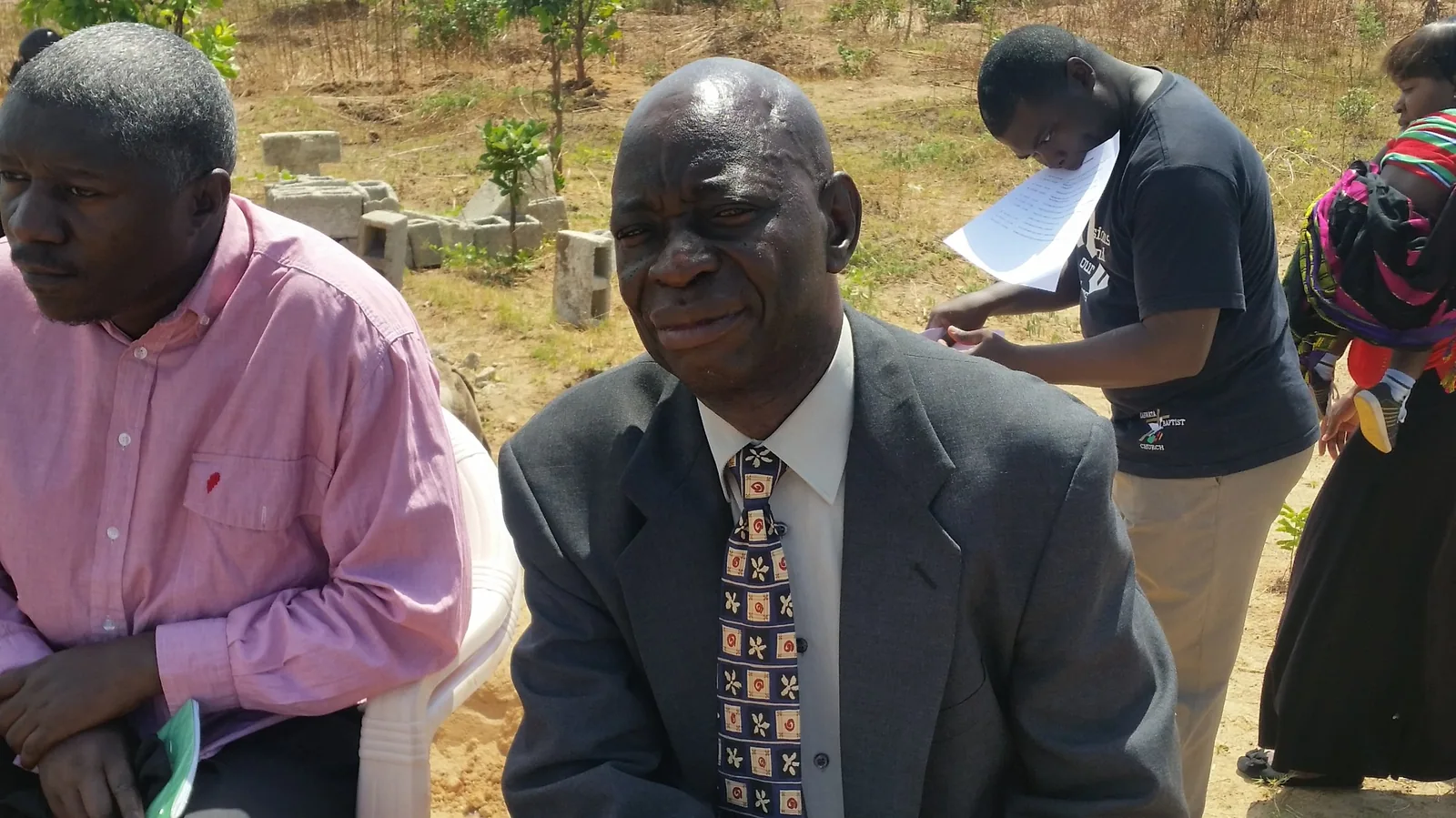 Two Zambian pastors seated together during an outdoor church gathering