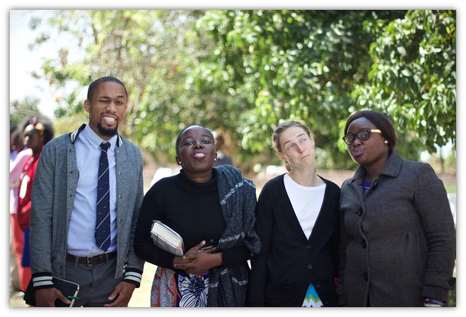 A pastor standing with several church members holding Bibles under a shade tree