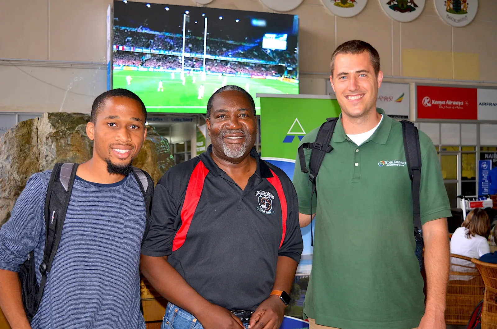 Three men, including visiting JPBC members, greeting one another at an airport in Zambia