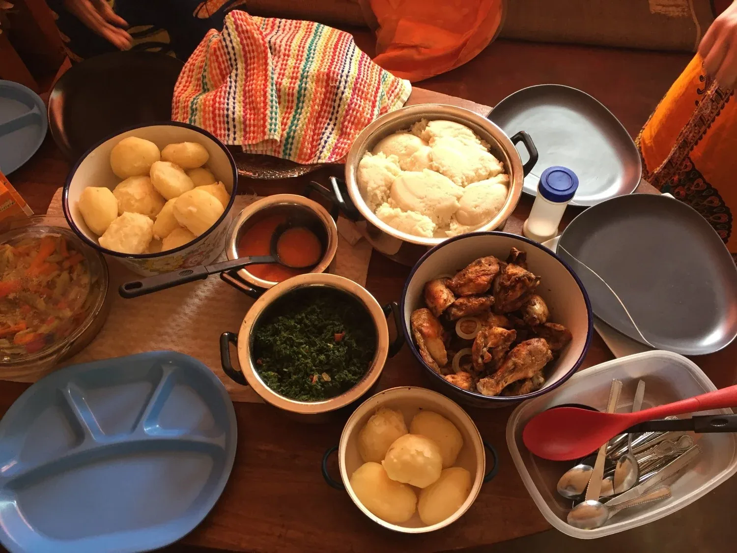 A shared Zambian meal of nshima, greens and stew laid out in bowls on a table