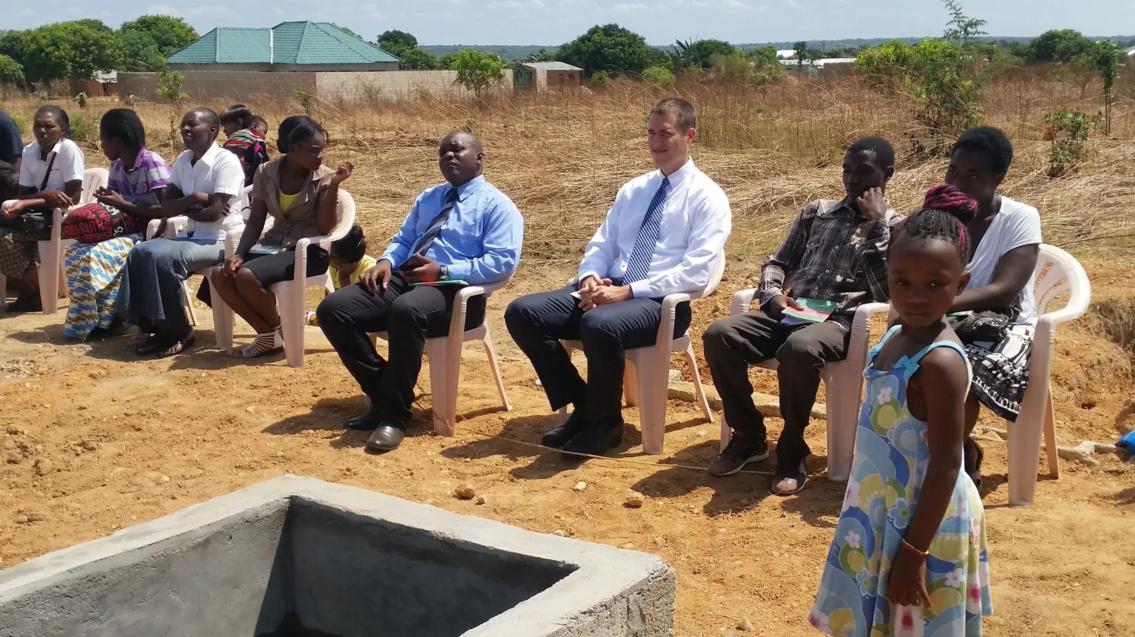 A congregation seated outdoors beside the baptismal pool for a baptism service