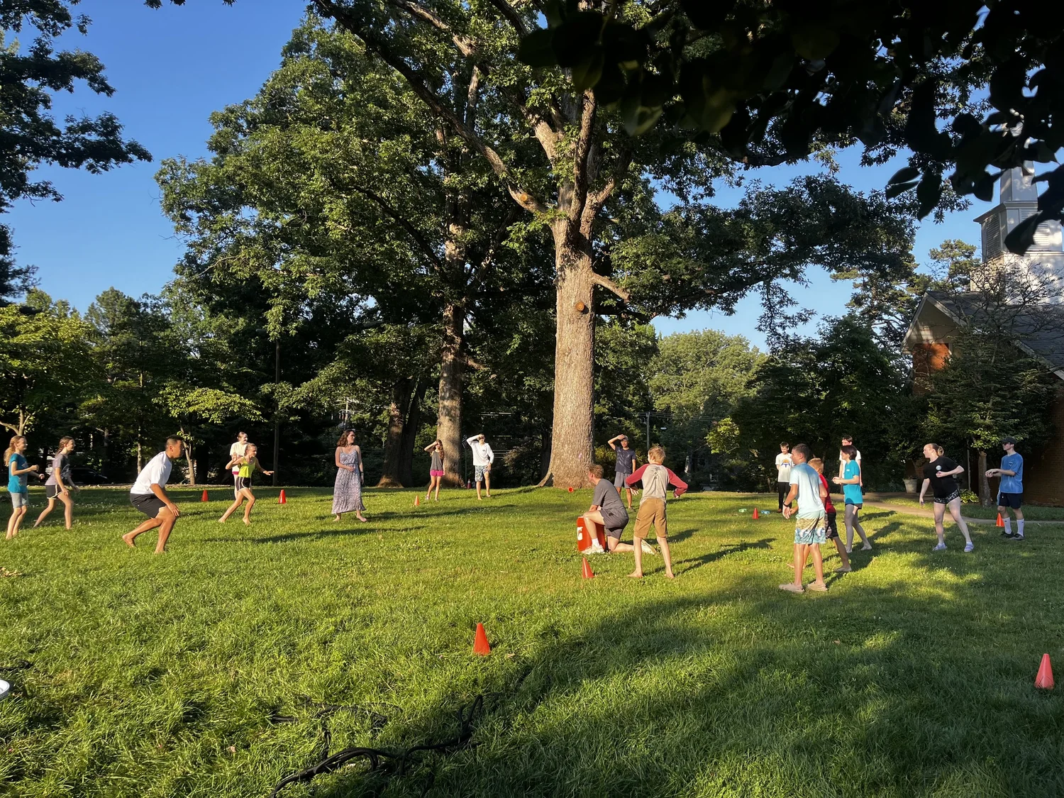 Kids and leaders playing a field game on the church lawn beside the steeple on a summer evening