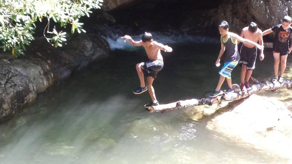 Boys crossing a fallen log over a mountain creek on a summer trip